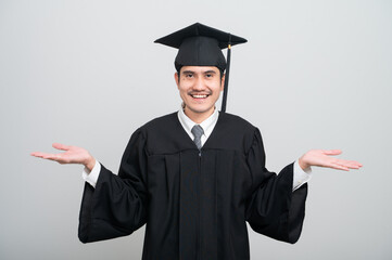 A young man in a graduation gown and cap smiles at the camera, striking a confident pose to...