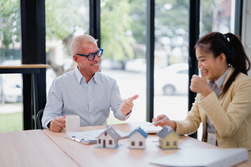 Real estate agent presenting house models to satisfied client giving a thumbs up during a...