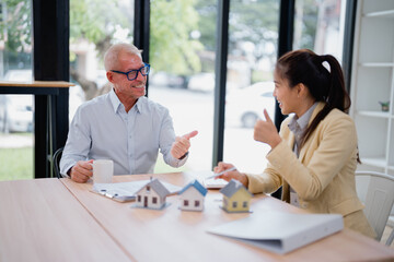 Real estate agent presenting house models to an enthusiastic client, who is smiling and giving a...