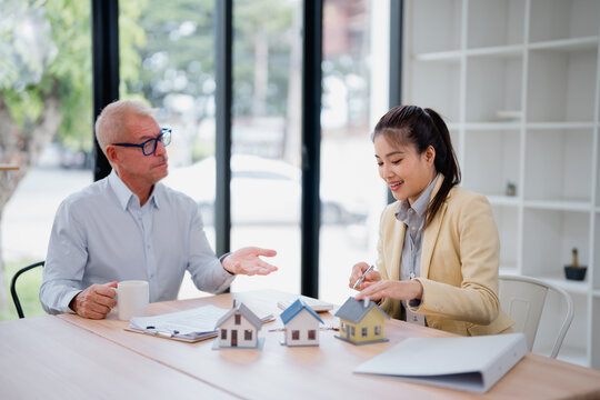 Real estate agent showing house models to potential buyer during a meeting in the office, discussing different options and investment opportunities