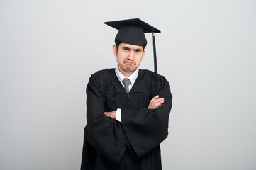 A young man in a graduation gown and cap smiles at the camera, striking a confident pose to...
