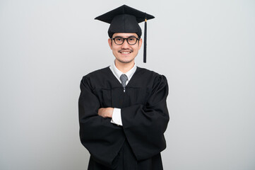 A young man in a graduation gown and cap smiles at the camera, striking a confident pose to...