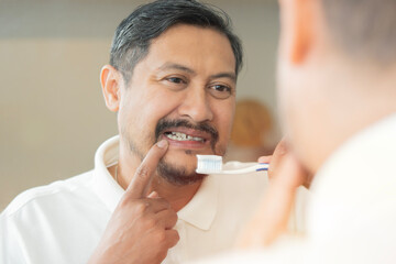 Man with aching teeth and brush while looking in mirror in bathroom.