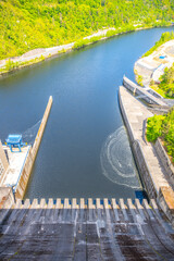 Looking down from the Orlik Dam in Czechia, the calm waters flow beneath, showcasing the engineering marvel of the hydroelectric power station and surrounding lush nature.