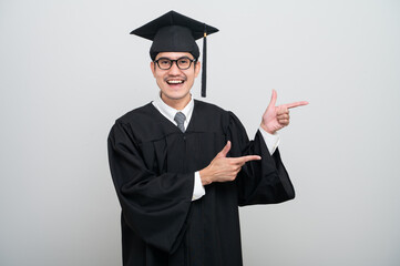 A young man in a graduation gown and cap smiles at the camera, striking a confident pose to...