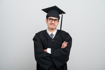 A young man in a graduation gown and cap smiles at the camera, striking a confident pose to...