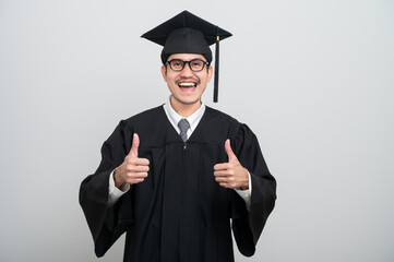 A young man in a graduation gown and cap smiles at the camera, striking a confident pose to...
