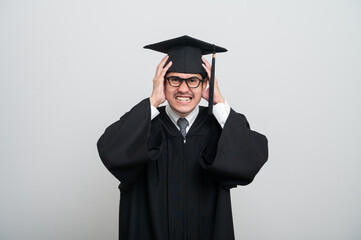 A young man in a graduation gown and cap smiles at the camera, striking a confident pose to...