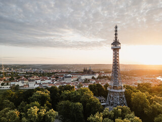 At sunrise, the Petrin Lookout Tower stands tall amid lush trees, providing a breathtaking view of Prague Castle and the city bathed in golden light. A serene start to the day. © pyty