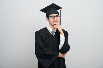 A young man in a graduation gown and cap smiles at the camera, striking a confident pose to...