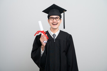 A young man in a graduation gown and cap smiles at the camera, striking a confident pose to...