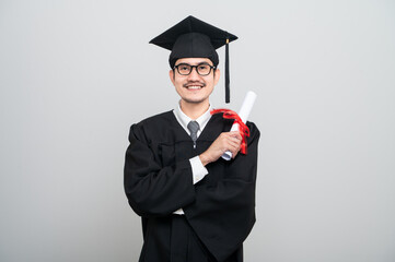 A young man in a graduation gown and cap smiles at the camera, striking a confident pose to...