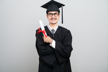 A young man in a graduation gown and cap smiles at the camera, striking a confident pose to...