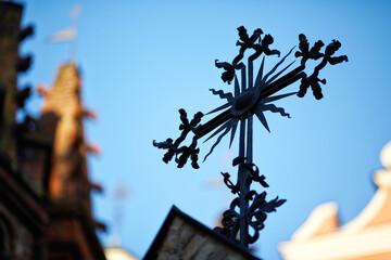 Ornate metal cross silhouette, blue sky background. Gothic architecture. Religious symbolism,...