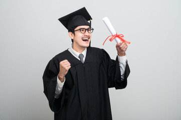 A young man in a graduation gown and cap smiles at the camera, striking a confident pose to...