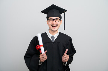 A young man in a graduation gown and cap smiles at the camera, striking a confident pose to...