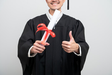 A young man in a graduation gown and cap smiles at the camera, striking a confident pose to...