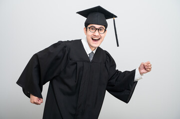 A young man in a graduation gown and cap smiles at the camera, striking a confident pose to...
