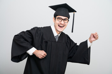 A young man in a graduation gown and cap smiles at the camera, striking a confident pose to...
