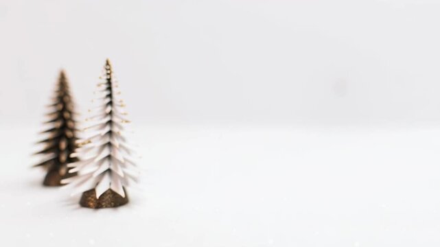 Two tiny decorative Christmas tree figures with glitter on a white snowy background for winter holiday footage.