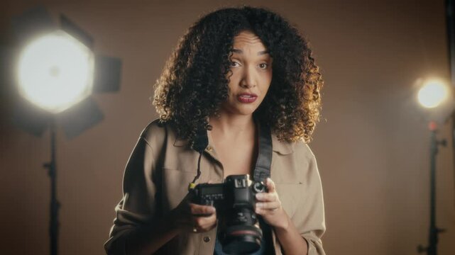a woman standing in a professional photography studio, taking a picture with a camera. She is surrounded by studio equipment, including large lights and a backdrop.