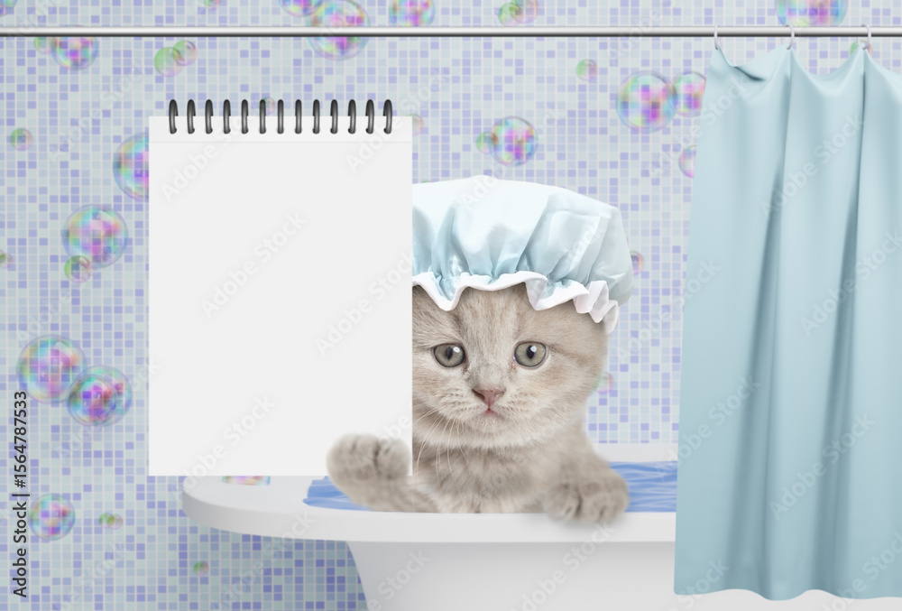 Poster cute gray kitten wearing shower cap takes the bath at home and shows blank white notepad in it paw. 