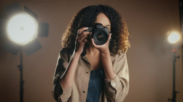 a woman standing in a professional photography studio, taking a picture with a camera. She is surrounded by studio equipment, including large lights and a backdrop. - Powered by Adobe