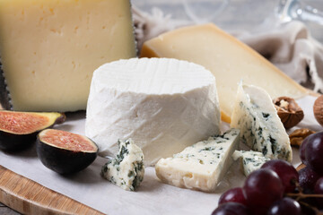 board of different cheeses with nuts, figs and grape on wooden table. Close up