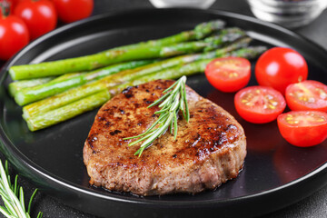 Close up, macro of tasty grilled beef steak served with green asparagus and cherry tomatoes on black plate, with cutlery. Perfect for food menu, diet, or culinary design concepts.