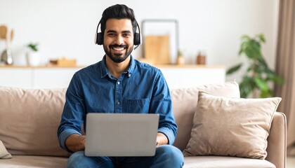 Portrait of a good-looking young Indian man using a laptop and earphones at home.