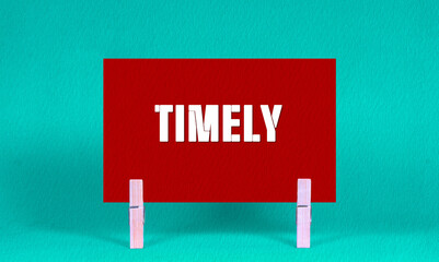 TIMELY Symbol. Concept words TIMELY on Red Rectangle Paper Held by Wooden Clothespin Green...