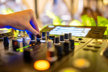 DJ adjusting knobs on a mixing console in a vibrant studio with colorful lights and display screen,...