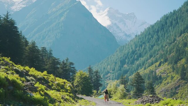 4K shot of solo female traveler walking on road leading towards epic mountains in Pangi Valley, India. Travel lifestyle concept adventure outdoor summer vacations. Active Indian young woman exploring 