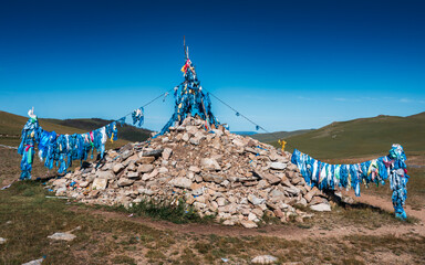 Mongolian ovoo with blue prayer flags under clear sky