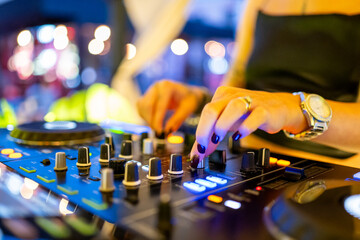 Close-up of a DJ adjusting knobs on a professional audio mixer with colorful stage lights, creating a dynamic and energetic party