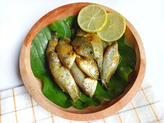 Marinated siamese gourami fish (Trichogaster pectoralis) on banana leaf and wooden plate with white background