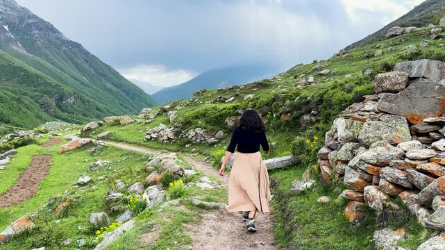 4K shot of young Indian woman walking on train in beautiful summer mountains in Sural Bhatori, Pangi Valley, India. Woman hiking in Himalayas mountains. Travel and holidays concept.
