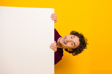 Happy young man in casual burgundy polo posing playfully holding a white panel against a vibrant...
