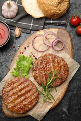 Delicious hamburger patties, tomatoes and spices on black table, flat lay