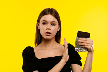 Woman Refusing a Chocolate Bar Against Bright Yellow Background