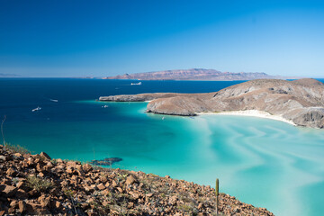 Captivating aerial view of Baja California's coastline, showcasing turquoise waters, rocky hills, and distant islands under a clear blue sky