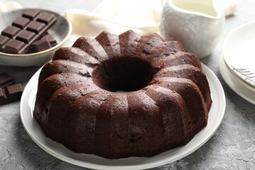 Tasty bundt cake and pieces of chocolate on grey table, closeup