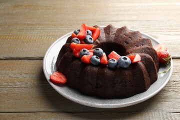 Tasty chocolate bundt cake with berries on wooden table