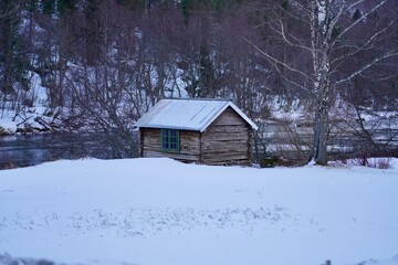 A small log cabin nestled between a snow covered field and the river Rauma in Romsdalen, Norway.