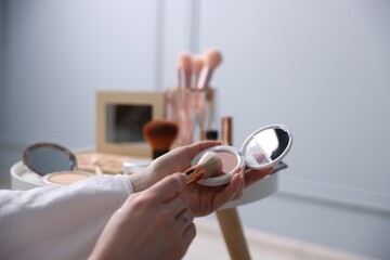 Woman with brush and powder at table indoors, closeup
