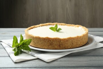 One tasty cheesecake with mint on grey table against wooden background, closeup