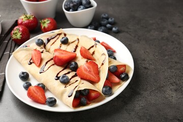 Tasty crepes with strawberries, blueberries and chocolate sauce on gray textured table, closeup