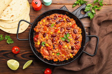 Tasty chili con carne in baking dish and flatbread on wooden table, flat lay