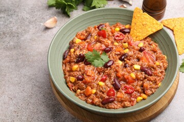 Tasty chili con carne in bowl and nachos on grey table, closeup. Space for text