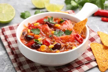 Tasty chili con carne in bowl and nachos on grey textured table, closeup